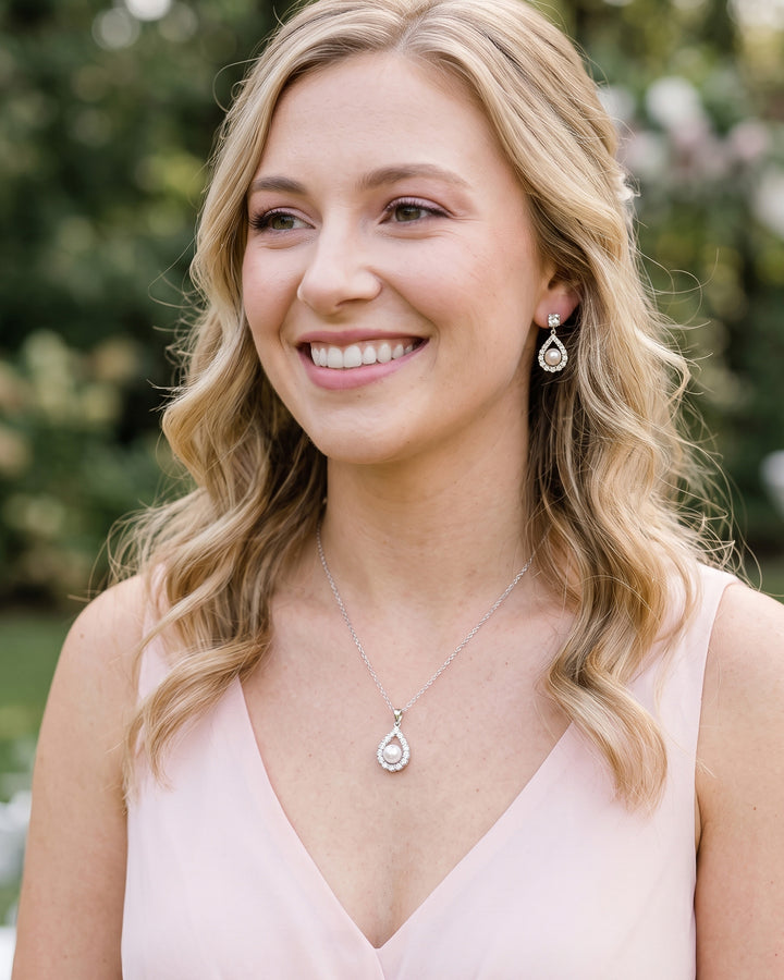 Smiling bridesmaid in a blush V-neck dress wearing the Elegance pearl drop earrings and necklace