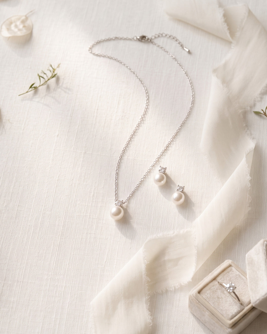 Justine silver pearl necklace and stud earrings laid flat on ivory linen