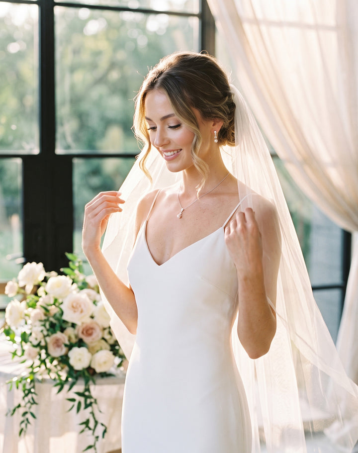 Bride by a window with a bouquet wearing the Kelsey pearl pendant set