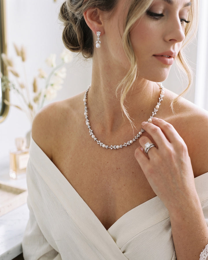Bride in an ivory wrap dress touching the Kelsey pearl and cubic zirconia necklace, with matching drop earrings