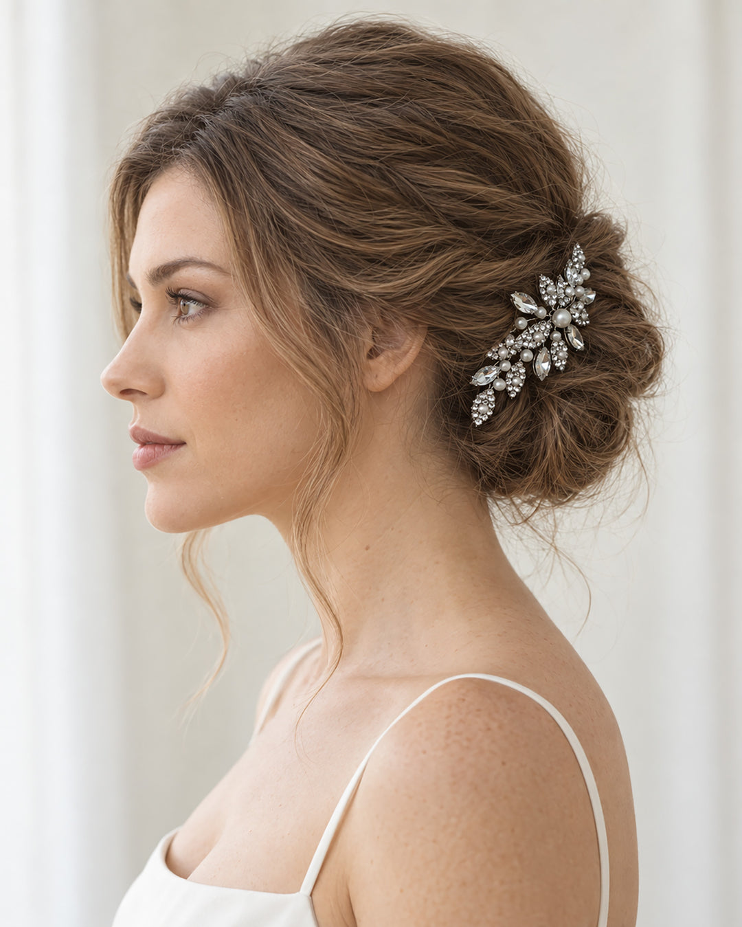 Side profile of a bride with an updo wearing a silver pearl and crystal hair comb