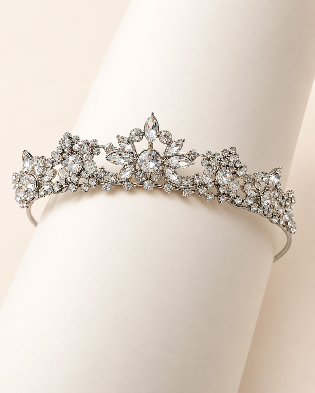 Silver rhinestone tiara with floral clusters draped over a hand showing the full design