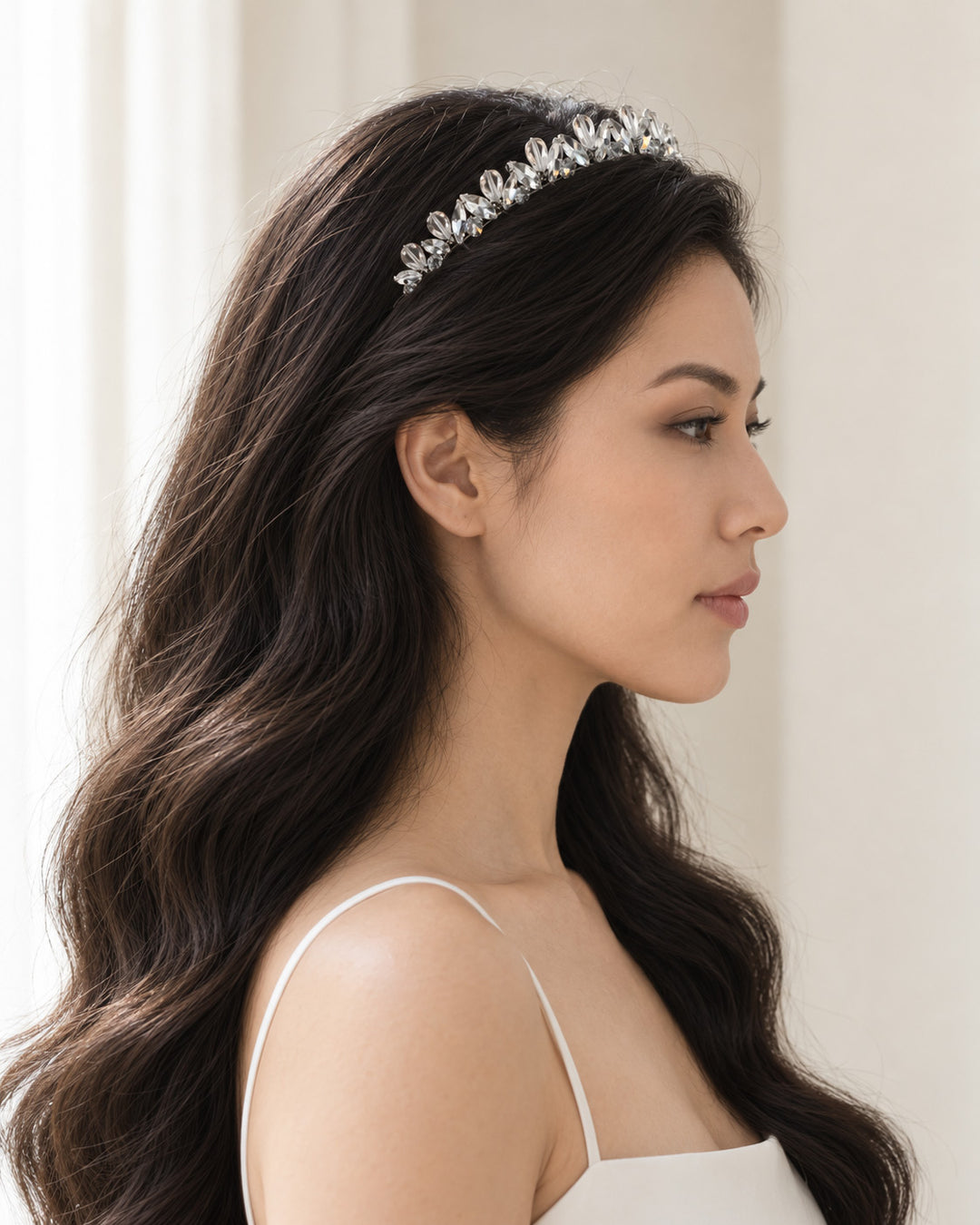 Side profile of a bridal look with long dark waves and a delicate silver crystal headband