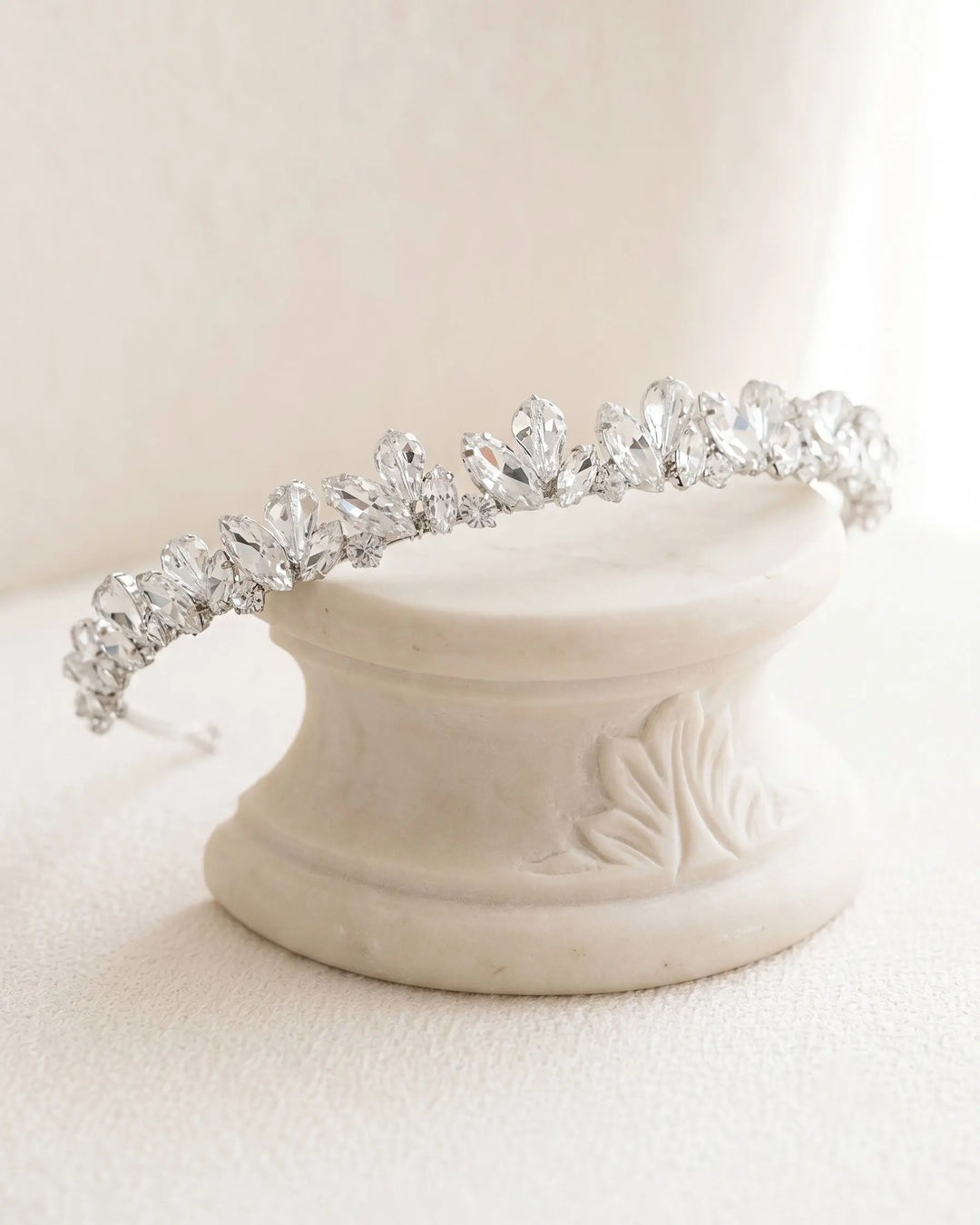Slim silver headband with a graduated crystal cluster resting on a cream marble pedestal