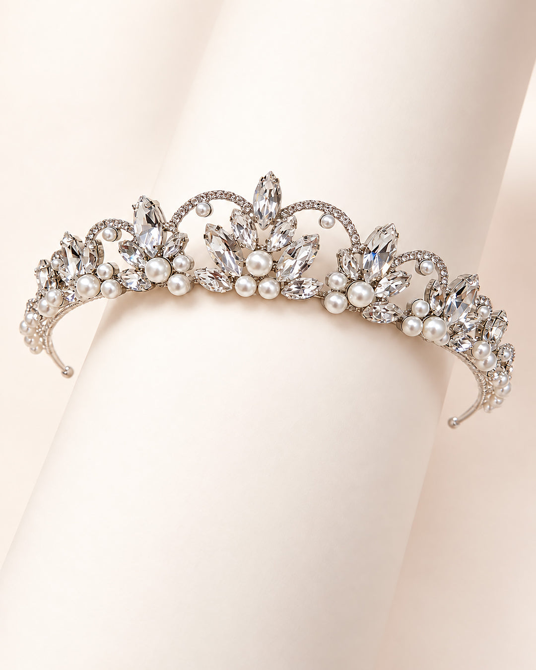 Close-up of a silver crown tiara with marquise rhinestone sprays and clustered pearls draped over a hand