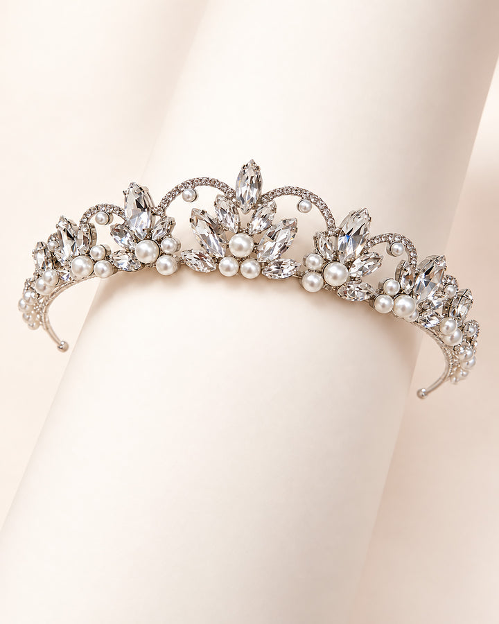 Close-up of a silver crown tiara with marquise rhinestone sprays and clustered pearls draped over a hand