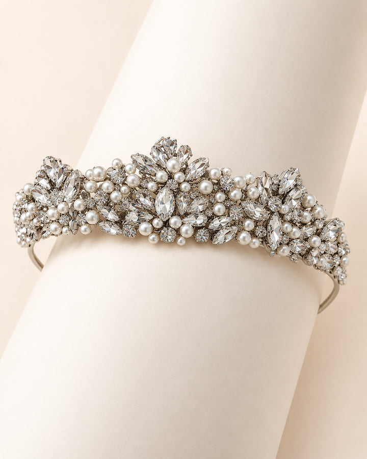 Close-up of a silver statement tiara wrapped around a hand showing dense pearl and rhinestone clusters