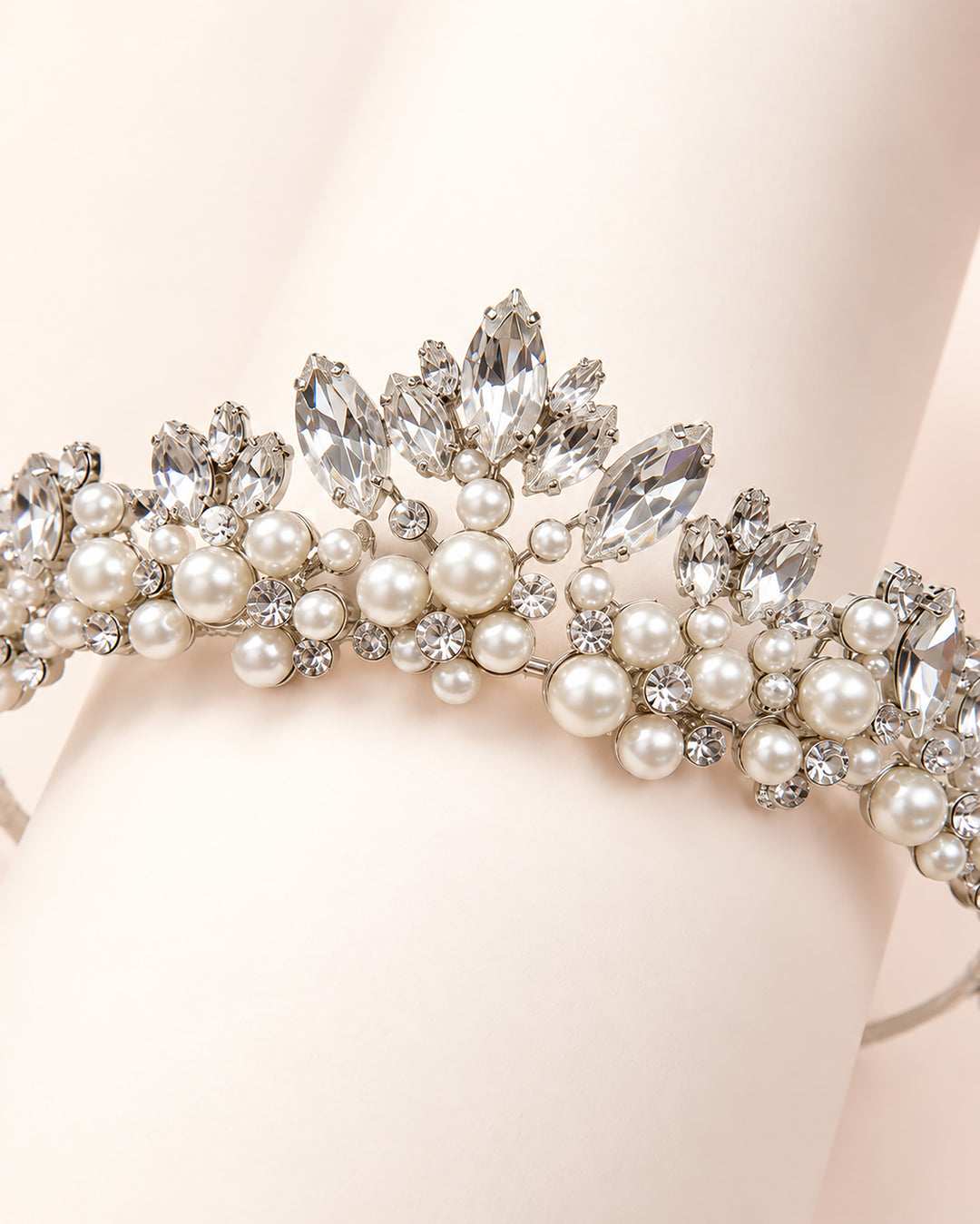 Close-up of a silver tiara with marquise rhinestones and clustered pearls draped over a hand