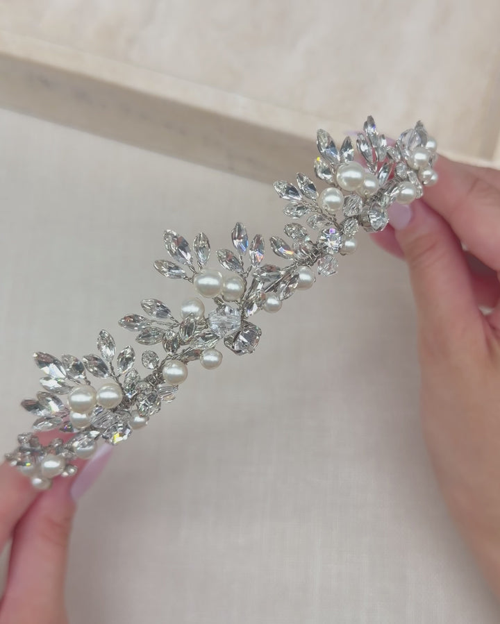 Hands holding the Amalie tiara to show its hand-wired rhinestone leaves, pearls and slim band