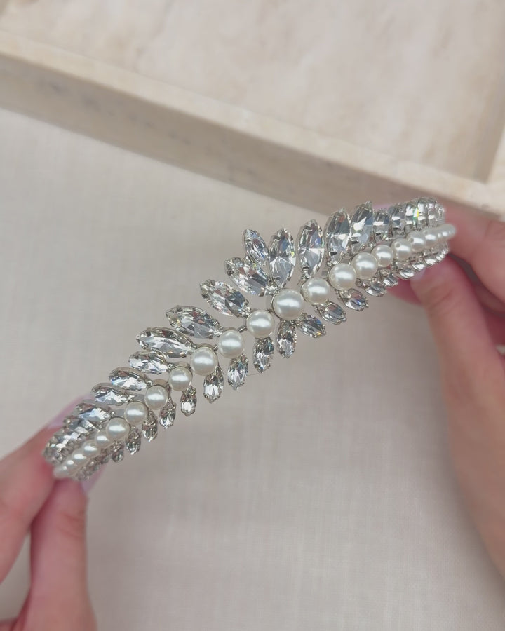 Hands holding the Mavis tiara to show its rows of rhinestones and ivory pearls up close