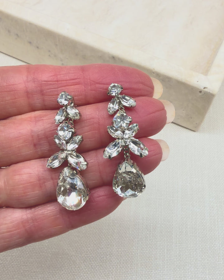 Hand holding the Tiana wedding earrings, turning them so the marquise crystals and teardrop catch the light