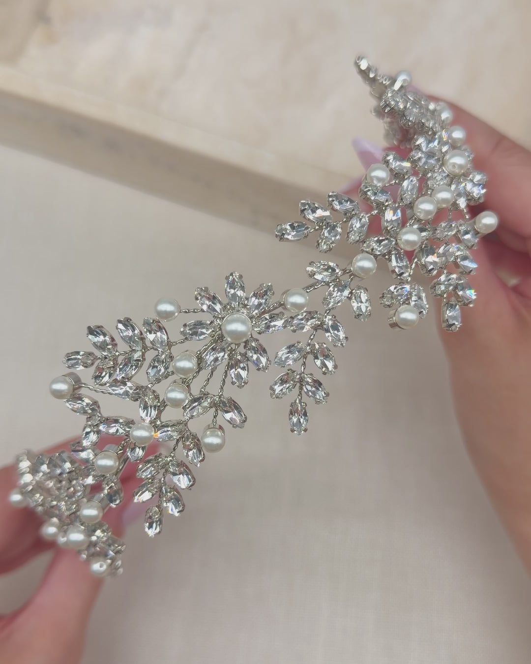 Hands holding the Liora headband to show its rhinestone leaves, blossoms and ivory pearls up close