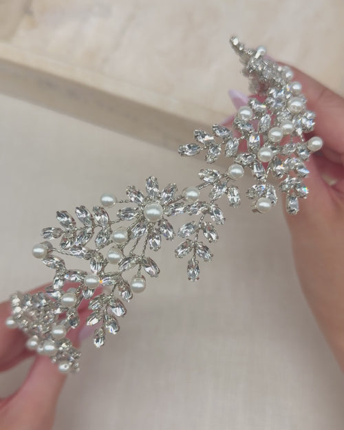 Hands holding the Liora headband to show its rhinestone leaves, blossoms and ivory pearls up close