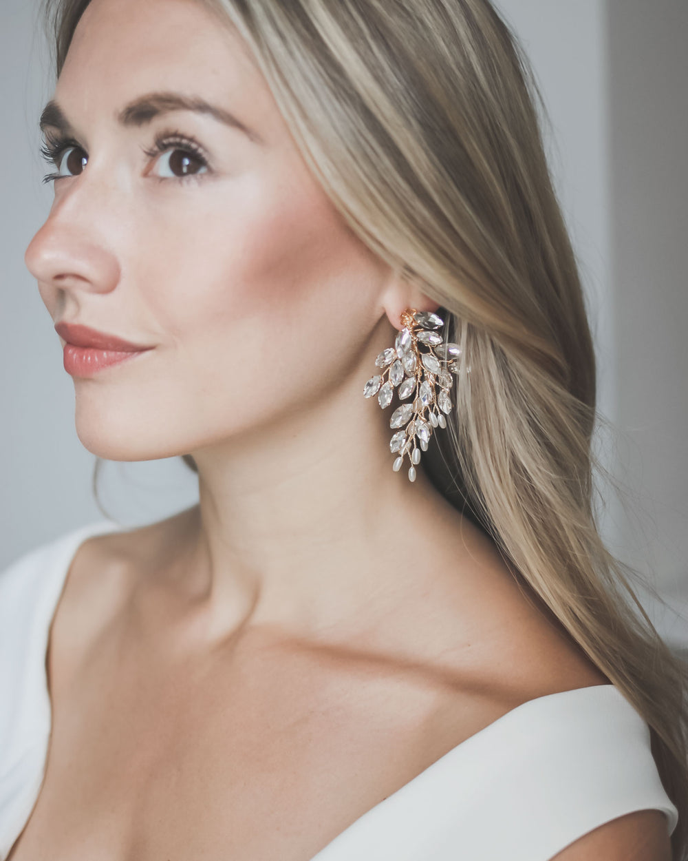 Gold Adria wedding earrings worn with sleek long hair, a branching spray of rhinestones and pearls